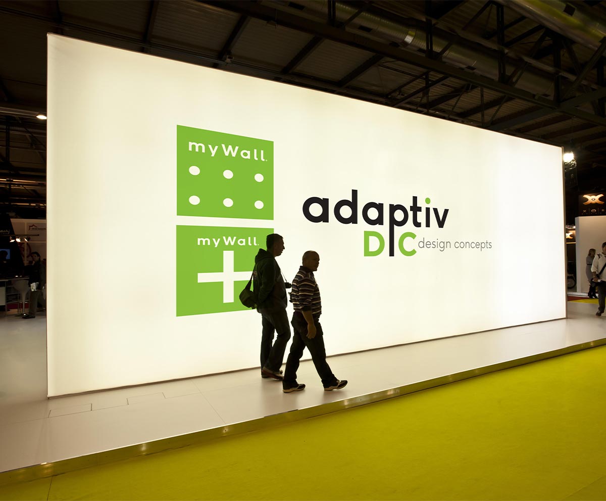 a large wall display with text that says, "adaptiv DC design concepts" with two people walking in front of it.